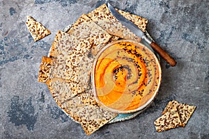 Pumpkin hummus seasoned with olive oil and black sesame seeds with whole grain crackers. Healthy vegetarian appetizer or snack.