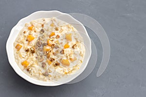 Pumpkin oatmeal with milk, honey and nuts on a gray stone background
