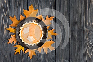 Pumpkin pie with cinnamon and cookies on black plate standing on autumn orange and brown tree leaves.