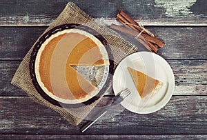 Pumpkin pie with cinnamon sticks on wooden table