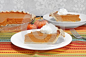 Pumpkin pie slice with whole pie in background.