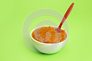 Pumpkin porridge in a bowl with a spoon on a green background, baby or vegan food. Copy space