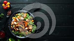 Pumpkin salad with chicken meat and vegetables in a black plate on a black background. Top view.