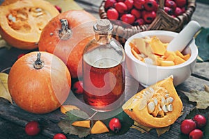 Pumpkin seeds oil bottle, pumpkins, mortar and basket of  hawthorn berries on wooden table.