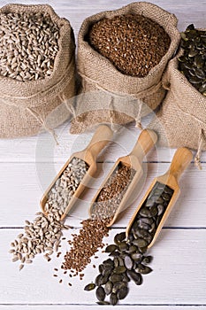 Pumpkin seeds, sunflower and flax seeds in wooden spoon. In the background jute bag with seeds.