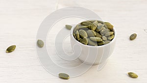 Pumpkin seeds in white bowl over wooden background close up