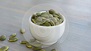 Pumpkin seeds in white bowl over wooden background close up