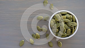 Pumpkin seeds in white bowl over wooden background top view