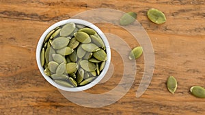 Pumpkin seeds in white bowl over wooden background top view