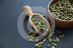 Pumpkin seeds in a wooden bowl and vintage scoop. Close up on a black background. copy space for text