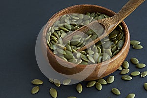 Pumpkin seeds in a wooden bowl and vintage scoop. Close up on a black background. copy space for text