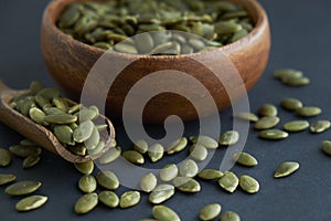 Pumpkin seeds in a wooden bowl and vintage scoop. Close up on a black background. copy space for text