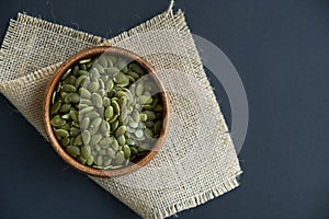 Pumpkin seeds in a wooden bowl and vintage scoop. Close up on a black background. copy space for text