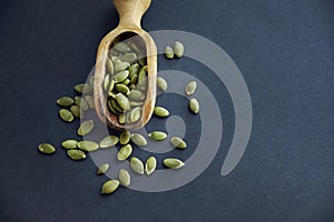 Pumpkin seeds in a wooden bowl and vintage scoop. Close up on a black background. copy space for text