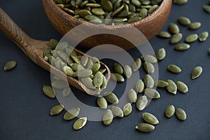 Pumpkin seeds in a wooden bowl and vintage scoop. Close up on a black background. copy space for text
