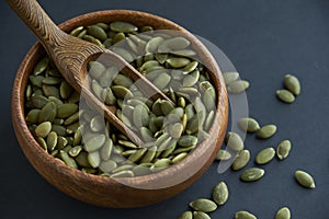 Pumpkin seeds in a wooden bowl and vintage scoop. Close up on a black background. copy space for text