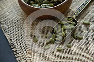 Pumpkin seeds in a wooden bowl and vintage scoop. Close up on a black background. copy space for text