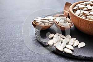 Pumpkin seeds and a wooden spoon on a dark table. Black slateboard with wooden bowl. Copy space