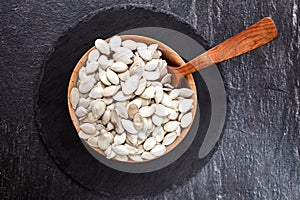 Pumpkin seeds and a wooden spoon on a dark table. Black slateboard with wooden bowl. Copy space