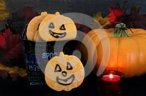 Pumpkin shaped cookies in a Halloween bucket in a fall setting, low light image with lit candle