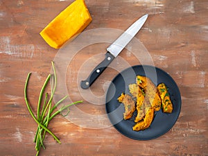 Pumpkin slices with aromatic herbs on a black plate, healthy food