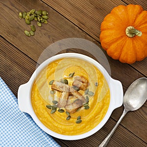 Pumpkin soup in a bowl,with fresh pumpkin seeds. Autumn foods. Healthy, vegetarian food, wooden background. Square image