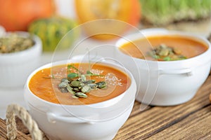 Pumpkin soup bowl with seeds on white wooden background. Close up