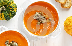 Pumpkin soup bowl with seeds on white wooden background. Top view.
