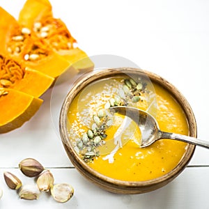 Pumpkin soup in a clay dish decorated with pumpkin seeds, sesame seeds, spices and cream