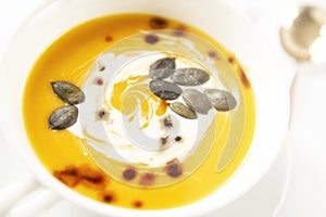 Pumpkin soup close-up in out of focus. Background image.Seasonal food.Soup decorated with cream sauce and pumpkin seeds