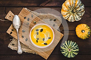 Pumpkin soup with cream and pumpkin seeds on dark brown rustic wooden background