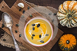 Pumpkin soup with cream and pumpkin seeds on a wooden board on dark brown rustic wooden background