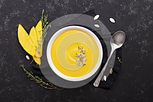 Pumpkin soup decorated seeds and thyme in white bowl on vintage black table top view. Flat lay styling.