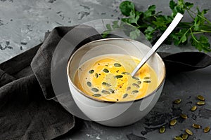 Pumpkin soup in deep bowl with seeds and spoon served with napkin and fresh green