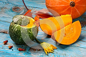 Pumpkin soup with fresh pumpkins, garlic and herbs presented in green pumpkin on a blue wooden background