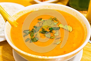 Pumpkin soup with green herb in white bowl on table in cafe