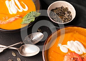 Pumpkin soup with shrimps, pumpkin seeds in dark bowls