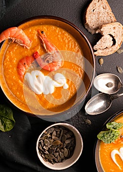 Pumpkin soup with shrimps, pumpkin seeds in dark bowls and silver spoons