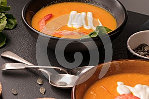 Pumpkin soup with shrimps, sour in dark bowls and bread, greenery and spoons
