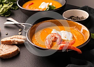 Pumpkin soup with shrimps, sour, pumpkin seeds in dark bowls and bread, greenery, silver spoons