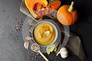 Pumpkin soup with wheat rusks and fresh pumpkins, garlic and spices in spoon on linen cloth over dark grunge background