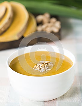 Pumpkin soup in white bowl with pine nut