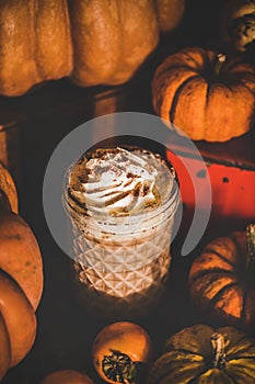 Pumpkin spice latte coffee drink in tall glass among pumpkins