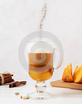 Pumpkin spice latte in a glass mug, cinnamon powder falling