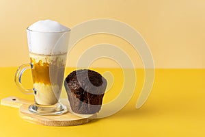 Pumpkin Spice Latte in a Glass Mug with Cinnamon on Wooden Cutting Board Chocolate Muffin Tasty Autumn Drink Yellow Background