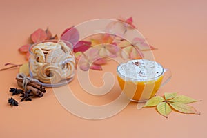 Pumpkin spice latte in a glass mug with whipped cream on  beige background. Autumn leaves. Hot autumn drink.