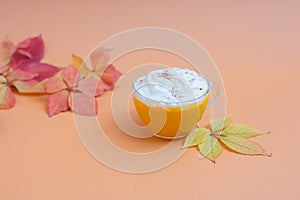 Pumpkin spice latte in a glass mug with whipped cream on  beige background. Autumn leaves. Hot autumn drink.