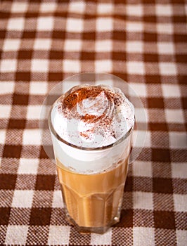 Pumpkin spice whipped latte in glass. Hot autumn drink beverage on checkered tablecloth