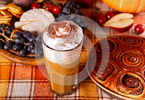 Pumpkin spice whipped latte in glass. Hot autumn drink beverage. Nearby delicious pie and appetizers fruits and cheese