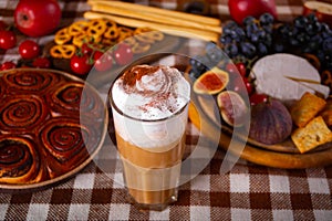 Pumpkin spice whipped latte in glass. Hot autumn drink beverage. Nearby delicious pie and appetizers fruits and cheese